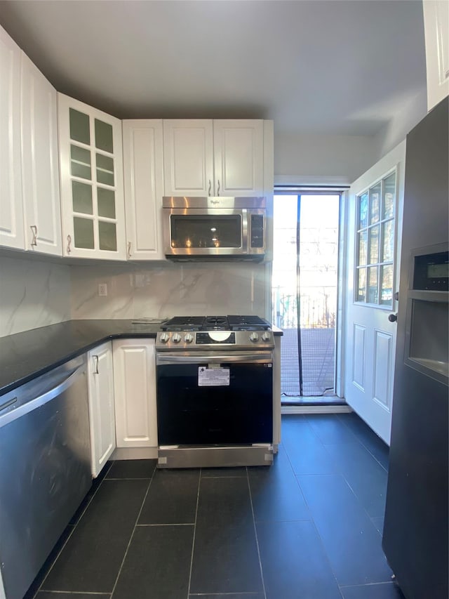 kitchen with tasteful backsplash, white cabinetry, dark tile patterned floors, and appliances with stainless steel finishes