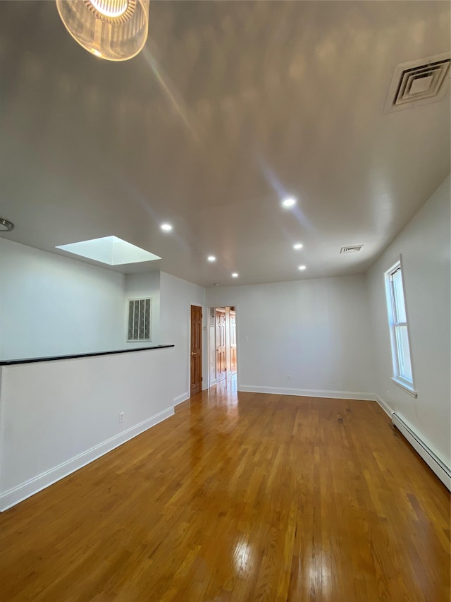 unfurnished room with a skylight, wood-type flooring, and a baseboard heating unit