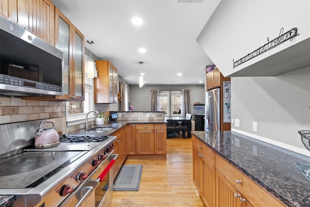 kitchen featuring kitchen peninsula, light hardwood / wood-style flooring, pendant lighting, appliances with stainless steel finishes, and sink