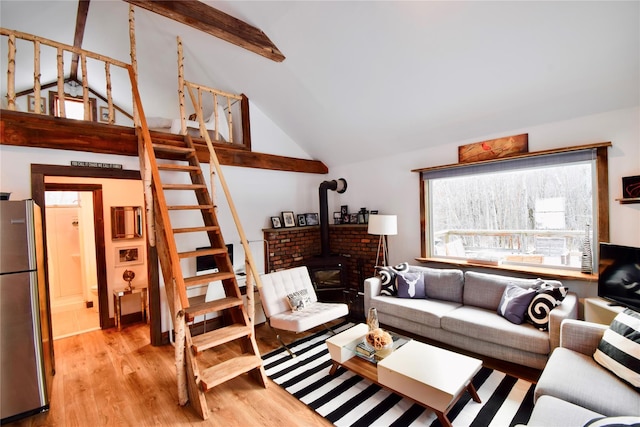 living room with vaulted ceiling with beams, light wood-type flooring, and a wood stove