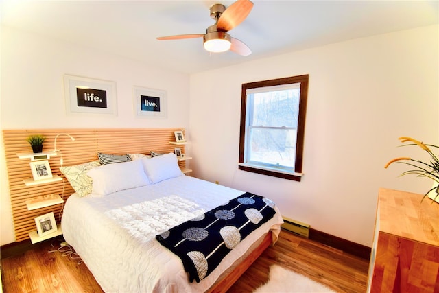 bedroom with ceiling fan, hardwood / wood-style floors, and a baseboard heating unit