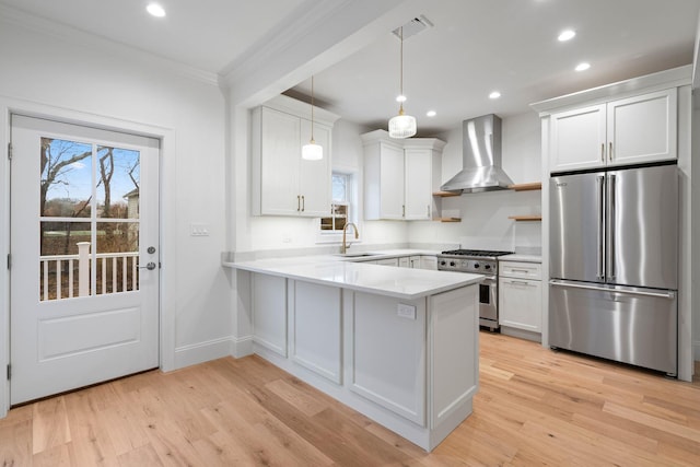 kitchen featuring premium appliances, a peninsula, a sink, light countertops, and wall chimney exhaust hood