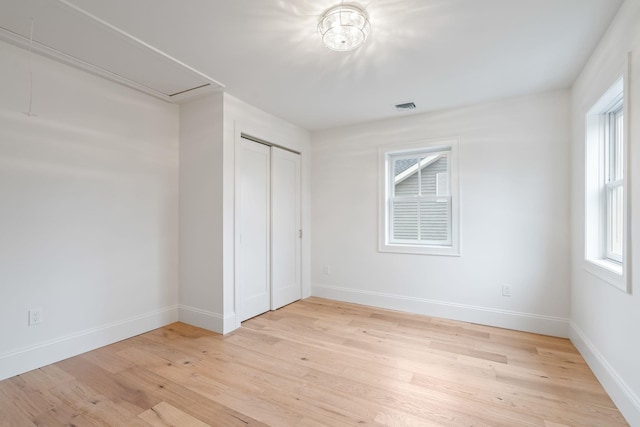 unfurnished bedroom with a closet, visible vents, light wood-style flooring, attic access, and baseboards