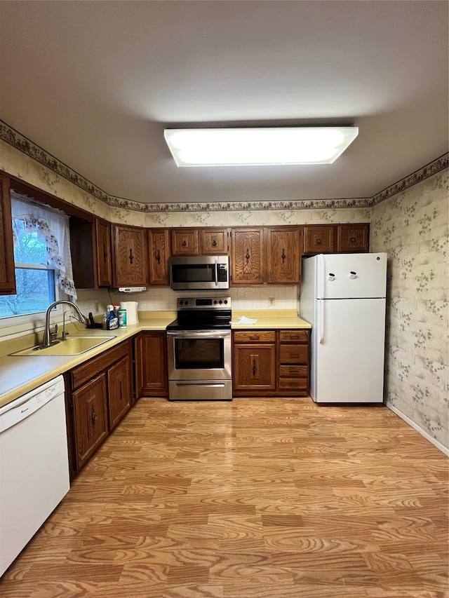 kitchen with backsplash, sink, light hardwood / wood-style floors, and appliances with stainless steel finishes