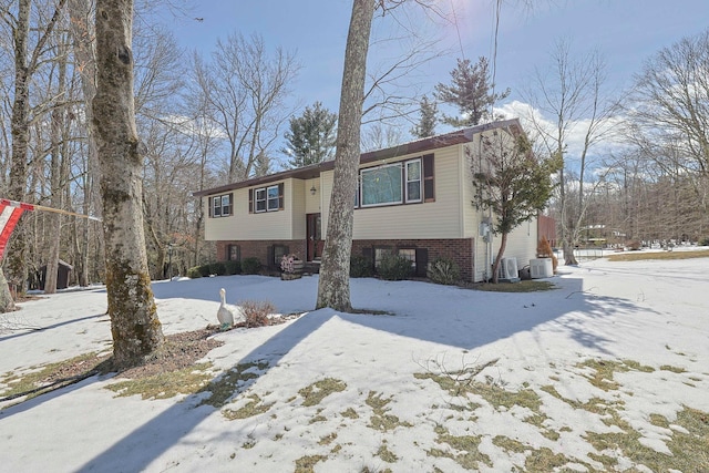 split foyer home with a garage, central AC unit, and brick siding