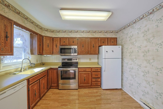 kitchen featuring a sink, light wood-style floors, appliances with stainless steel finishes, brown cabinets, and wallpapered walls