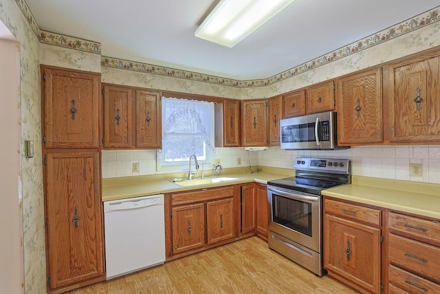 kitchen featuring light wood finished floors, appliances with stainless steel finishes, brown cabinetry, and a sink