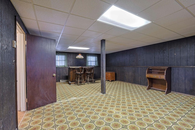 basement featuring a bar, wooden walls, a baseboard heating unit, and tile patterned floors