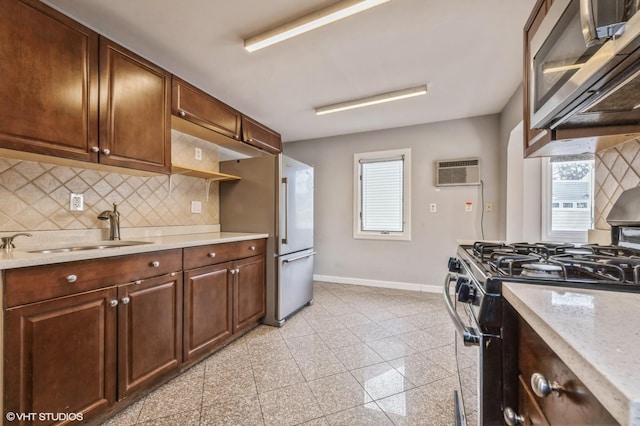 kitchen featuring backsplash, sink, appliances with stainless steel finishes, light stone counters, and a wall unit AC