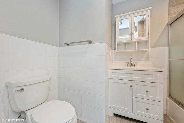 full bathroom featuring combined bath / shower with glass door, vanity, toilet, and tile walls