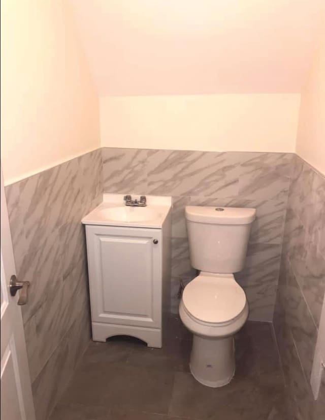 bathroom featuring tile patterned flooring, vanity, toilet, and tile walls