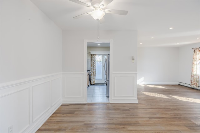 spare room with baseboard heating, ceiling fan, and light hardwood / wood-style floors