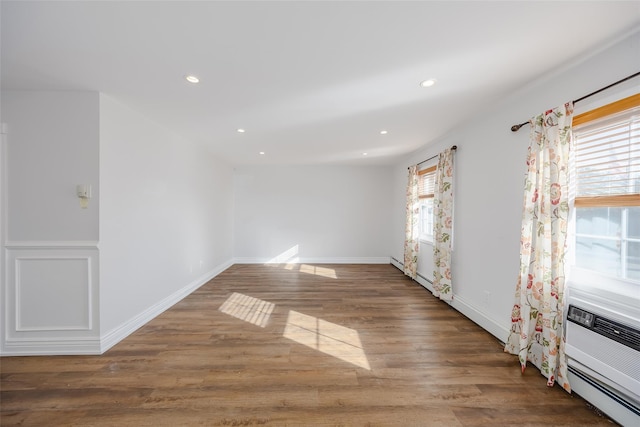 unfurnished room featuring dark hardwood / wood-style flooring, baseboard heating, and a healthy amount of sunlight