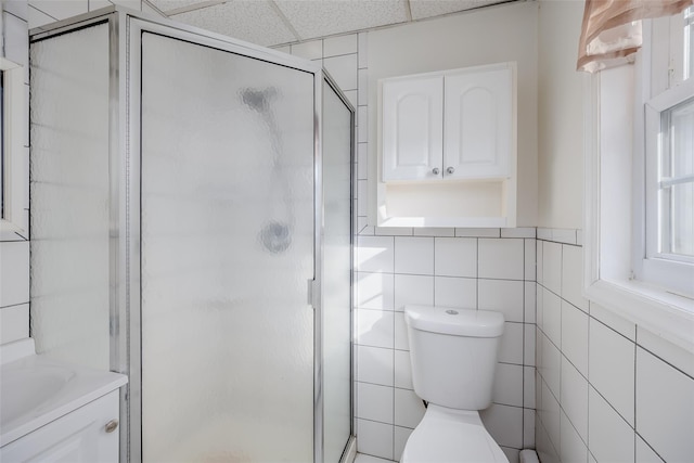 bathroom with a drop ceiling, vanity, tile walls, and walk in shower