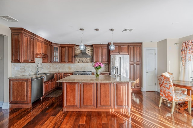 kitchen featuring sink, a center island, hanging light fixtures, appliances with stainless steel finishes, and wall chimney range hood