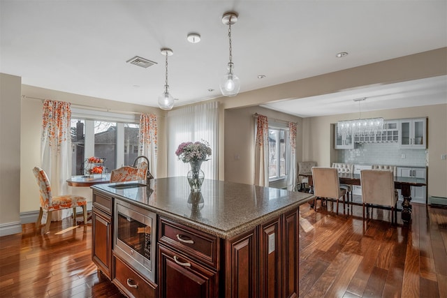 kitchen with sink, hanging light fixtures, stainless steel microwave, dark hardwood / wood-style flooring, and a kitchen island