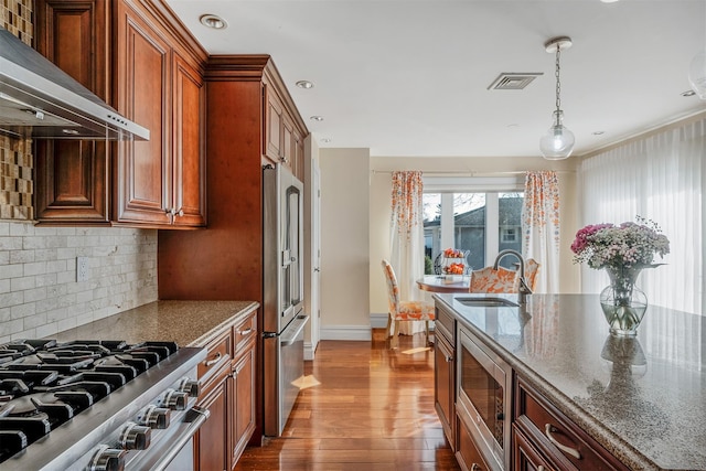 kitchen featuring sink, decorative light fixtures, dark stone countertops, stainless steel appliances, and wall chimney range hood