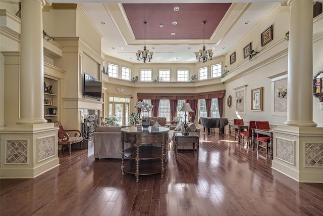 interior space featuring a notable chandelier, dark wood-style floors, a tray ceiling, decorative columns, and crown molding