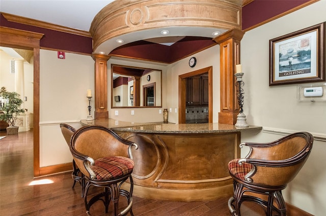 bar with wood-type flooring, ornate columns, and dark stone countertops