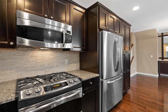 kitchen featuring dark brown cabinetry, tasteful backsplash, appliances with stainless steel finishes, light stone counters, and dark wood-type flooring