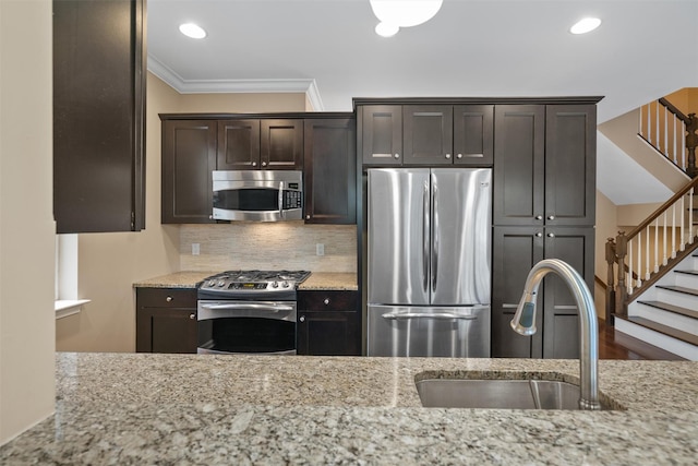 kitchen with crown molding, appliances with stainless steel finishes, a sink, dark brown cabinetry, and light stone countertops