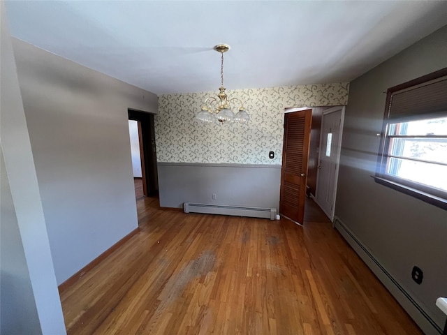 unfurnished dining area with wood-type flooring, a notable chandelier, and a baseboard heating unit