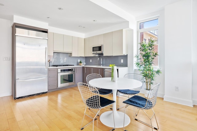 kitchen featuring light wood-type flooring, stainless steel appliances, gray cabinets, and backsplash