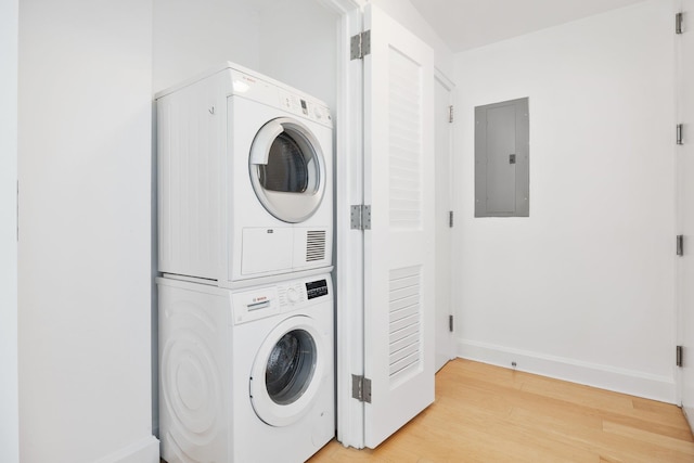 clothes washing area with electric panel, stacked washer and dryer, and light hardwood / wood-style floors