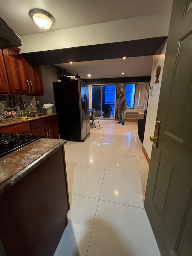 kitchen with exhaust hood, black refrigerator with ice dispenser, dark stone counters, sink, and light tile patterned flooring