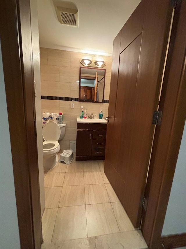 bathroom featuring tile patterned flooring, vanity, toilet, and tile walls