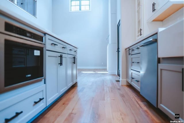 kitchen with stainless steel oven, light wood-type flooring, and white cabinetry