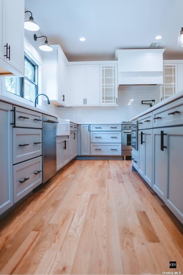 kitchen featuring white cabinetry, stainless steel appliances, light hardwood / wood-style floors, decorative light fixtures, and decorative backsplash