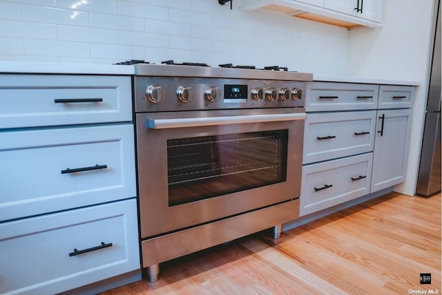 kitchen featuring high end stove, white cabinetry, tasteful backsplash, and light hardwood / wood-style floors