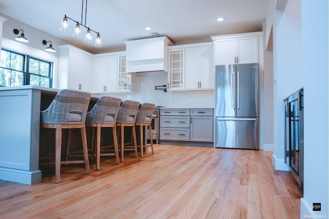 kitchen featuring white cabinets, a kitchen breakfast bar, stainless steel appliances, and custom exhaust hood