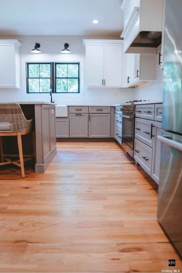 kitchen featuring gray cabinetry, white cabinetry, stainless steel appliances, premium range hood, and light hardwood / wood-style floors