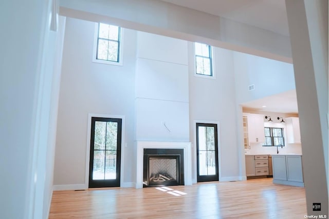 unfurnished living room featuring a towering ceiling, light hardwood / wood-style flooring, and a healthy amount of sunlight