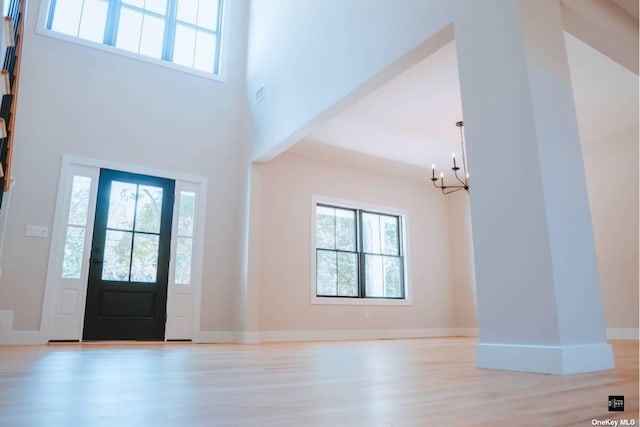 entryway with light wood-type flooring, a towering ceiling, a chandelier, and a healthy amount of sunlight