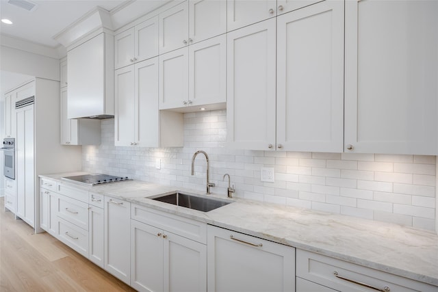 kitchen with sink, light stone counters, stovetop, decorative backsplash, and white cabinets