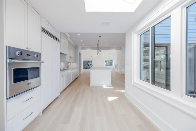 kitchen with white cabinets, decorative light fixtures, a healthy amount of sunlight, and stainless steel oven