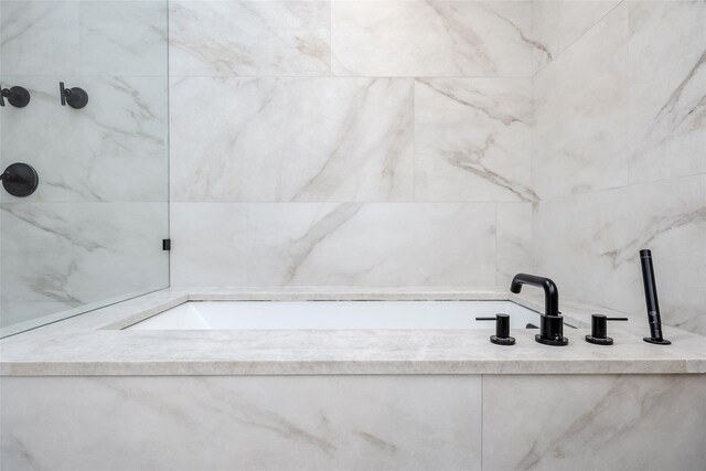 bathroom featuring a marble finish shower, a bath, and tile walls