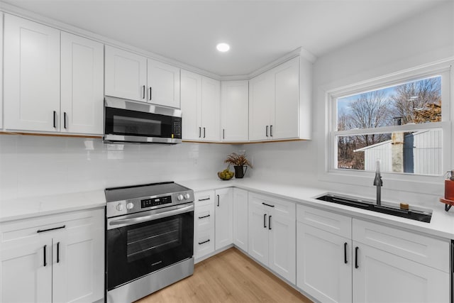 kitchen featuring white cabinetry, sink, light hardwood / wood-style flooring, backsplash, and appliances with stainless steel finishes