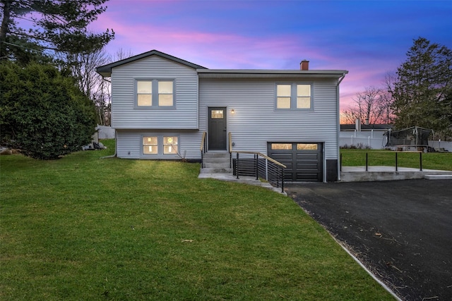 raised ranch featuring a garage and a yard