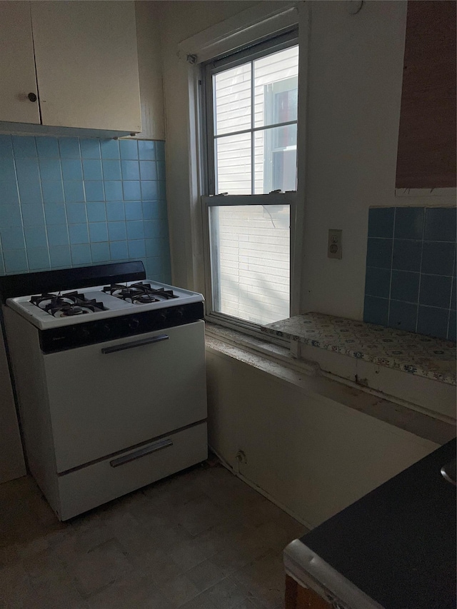 kitchen with backsplash, light stone counters, white cabinets, and white range with gas stovetop