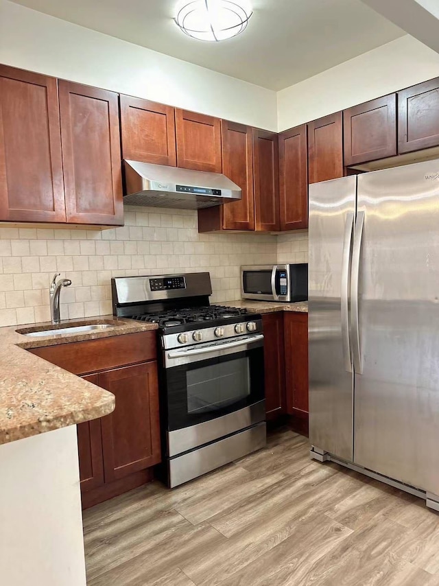 kitchen with sink, tasteful backsplash, light stone counters, light hardwood / wood-style flooring, and appliances with stainless steel finishes