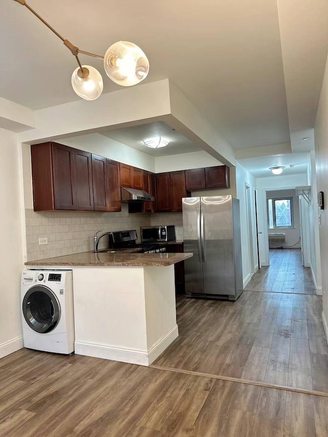 kitchen with appliances with stainless steel finishes, decorative backsplash, wood-type flooring, and washer / clothes dryer