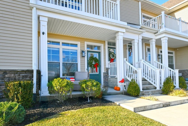 view of exterior entry featuring covered porch and a balcony