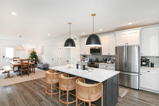 kitchen featuring white cabinets, a center island with sink, hanging light fixtures, dark hardwood / wood-style floors, and appliances with stainless steel finishes