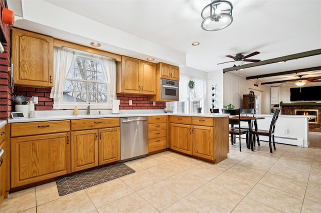 kitchen with appliances with stainless steel finishes, ceiling fan, sink, beamed ceiling, and a fireplace