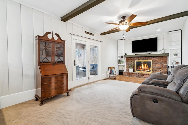 carpeted living room with ceiling fan, beam ceiling, and a brick fireplace