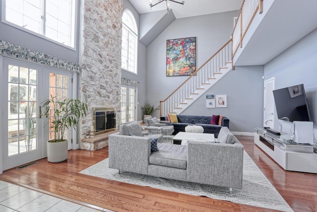 living room with a stone fireplace, wood-type flooring, and a high ceiling